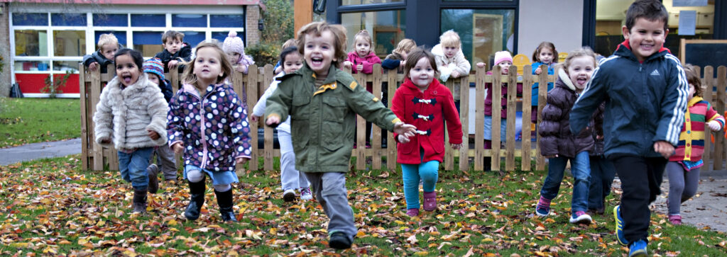 outside shot of young children in coats playing | Ducklings Nursery